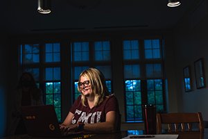 A women sits at kitchen table doing her online homework at night.
