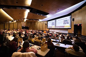 Students sit in a large conference hall at Central Michigan University to hear a panel speak on the importance of community partnerships in teaching.