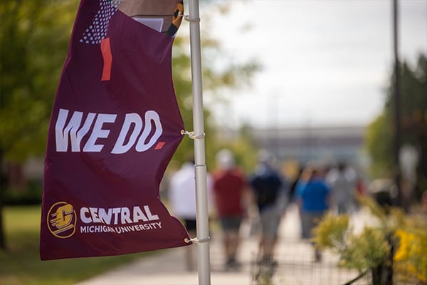 A maroon flag with the words We Do and Central Michigan University waves in the wind.