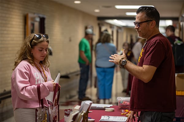 A future student in a pink sweatshirt talks with a faculty member at a visit event on campus.