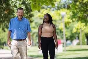 a man and woman walking together with green trees in the background