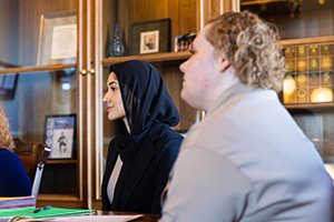 a woman in a black head scarf sitting at a table with a person in tan jacket