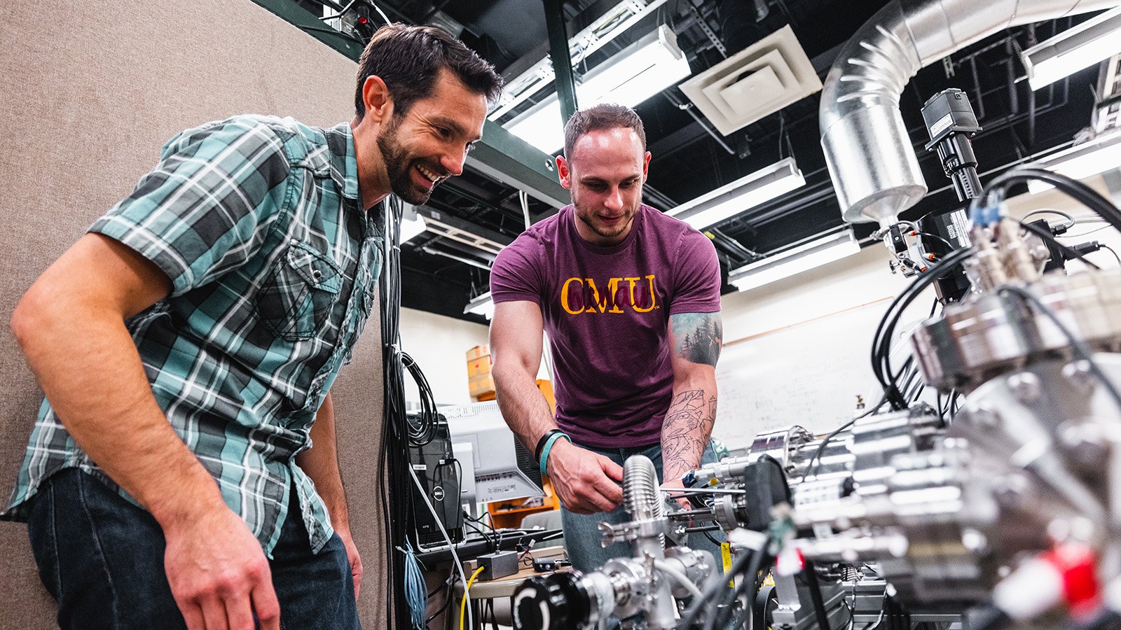 A male faculty with dark hair and a male student in a maroon shirt working on a research project.