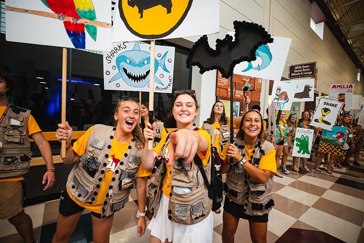 Students smile and point at the camera during Leadership Safari while holding signs featuring their team names.