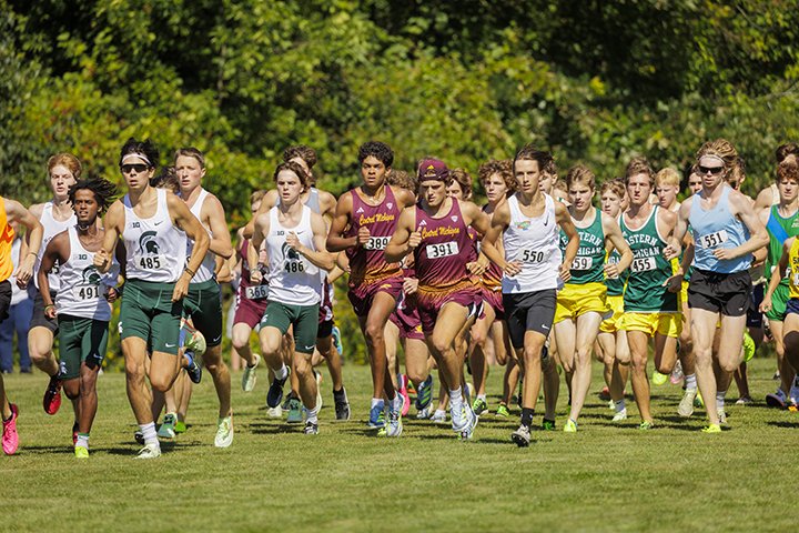 Dozens of men's cross country athletes run in a large group at the start of the race.