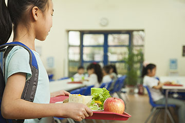 A girl carries a tray of food into a school cafeteria.