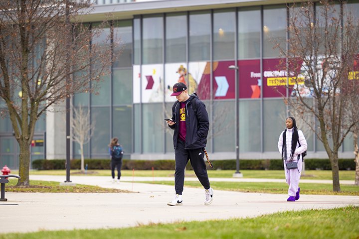 A student wearing a CMU hat and shirt looks at his phone while walking through campus on the first day back from winter break.