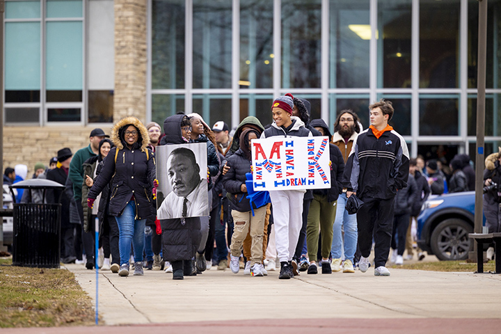 Hundreds of students march on a sidewalk carrying signs with Martin Luther King Jr.'s likeness and words from his "I have a dream" speech.