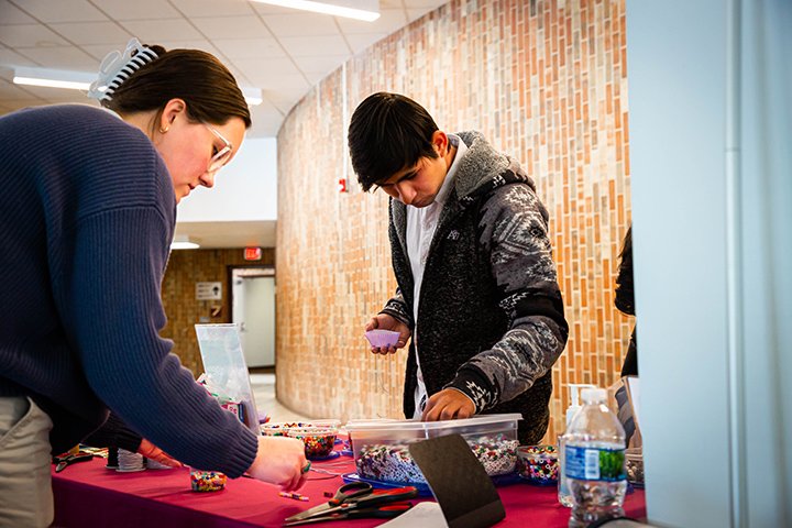 Students stand at a table covered with various items available for crafting.