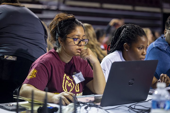 A female student wearing glasses and a maroon shirt stares at a computer screen during the ERPsim competition.
