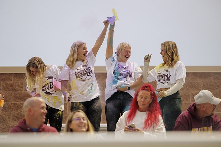 Four female soccer fans burst a colored powder packet on themselves, covering their white CMU t-shirts in various pastel colors.
