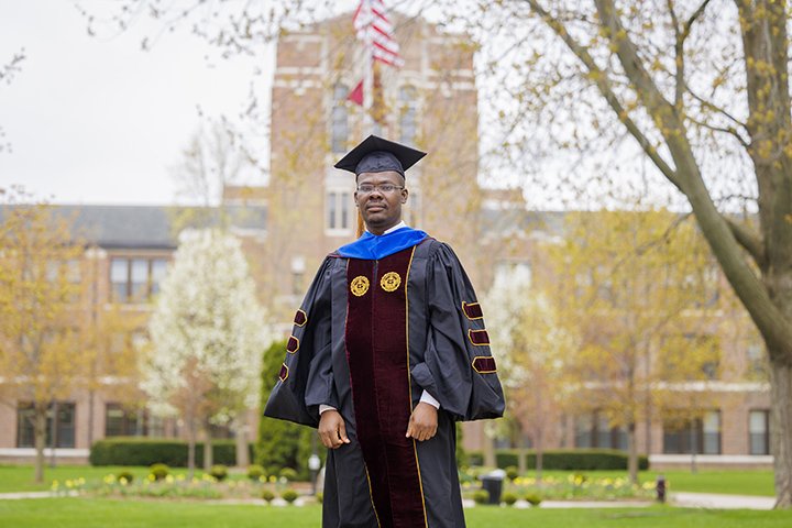 Nicholas Banahene wears his commencement attire while standing in front of Warriner Hall.