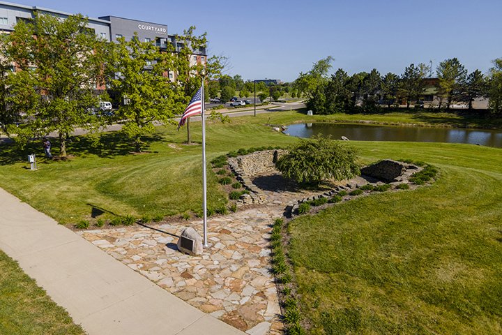 An aerial view of the Veterans Peace Grover featuring an American flag, rock path and a pond.