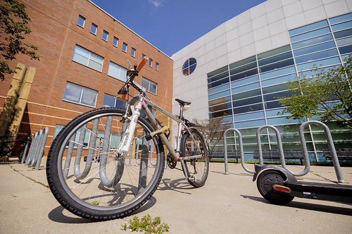A white and gray mountain bike and a scooter are parked near a bike rack outside of the Charles V. Park Library.