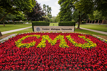 CMU is spelled in yellow flowers surrounded by a large group of red flowers in front of a cement sign that reads "Central Michigan University."