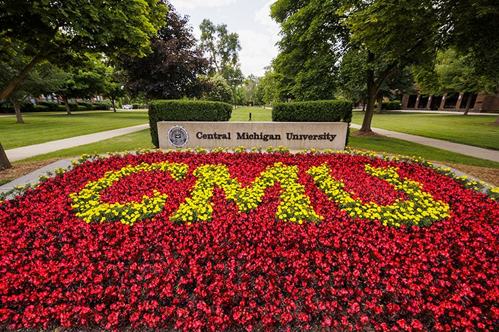 CMU is spelled in yellow flowers surrounded by a large group of red flowers in front of a cement sign that reads 