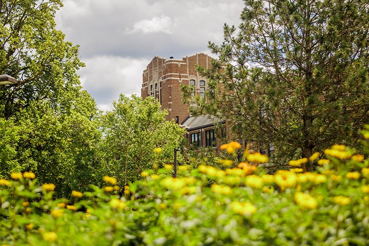Warriner Hall peeks through green trees and flowers on an overcast day.