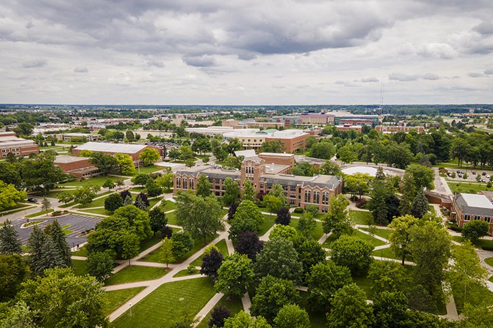 An aerial view of Central Michigan University's campus with gray skies, lush green trees and brick buildings.