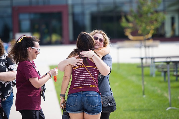Two women embrace on a sidewalk outside of Kelly/Shorts Stadium as a third woman stands next to them.