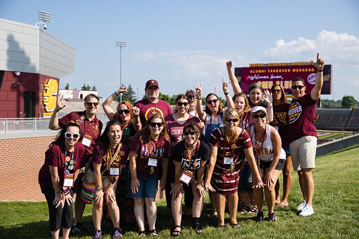 A group of 16 people wearing CMU apparel stand together for a group photo outside of Kelly/Shorts Stadium.