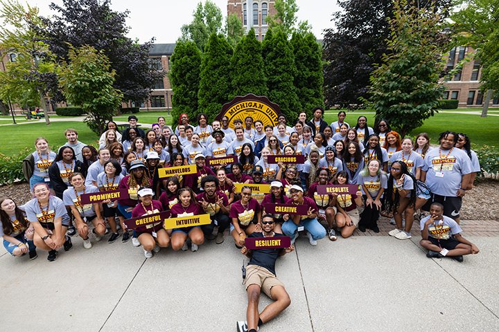A group of students taking part in IMPACT pose for a photo near the CMU seal in front of Warriner Hall.