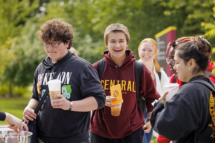 A group of four students stand in line holding drinks waiting to register to vote.