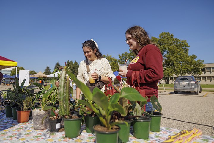 Two students stand at a table browsing plants for purchase.
