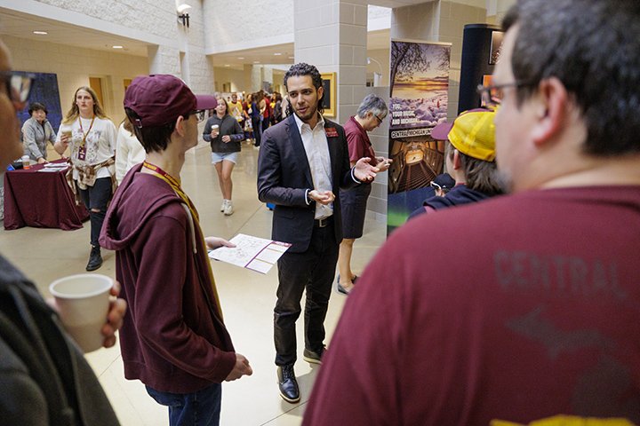 Prospective students dressed in maroon CMU apparel speak with a music department faculty member in a hallway.