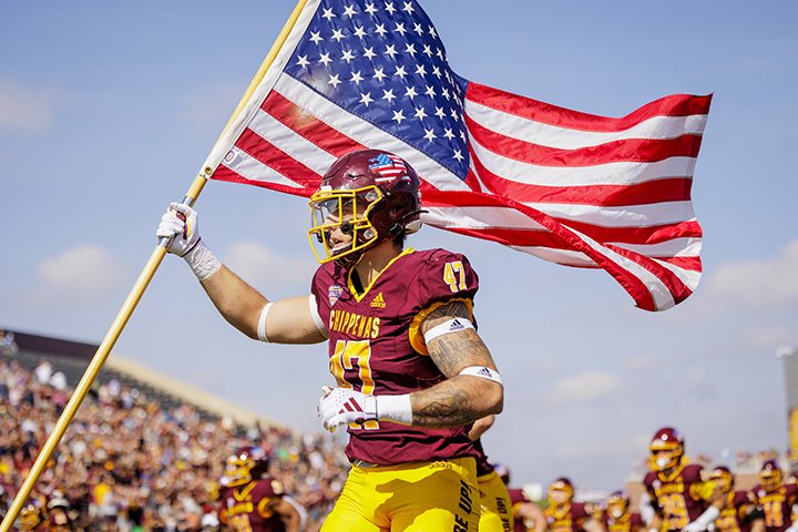 Junior tight end Bailey Smith carries the American flag in his left arm, leading the CMU football team onto the field prior to the game against Eastern Michigan University.