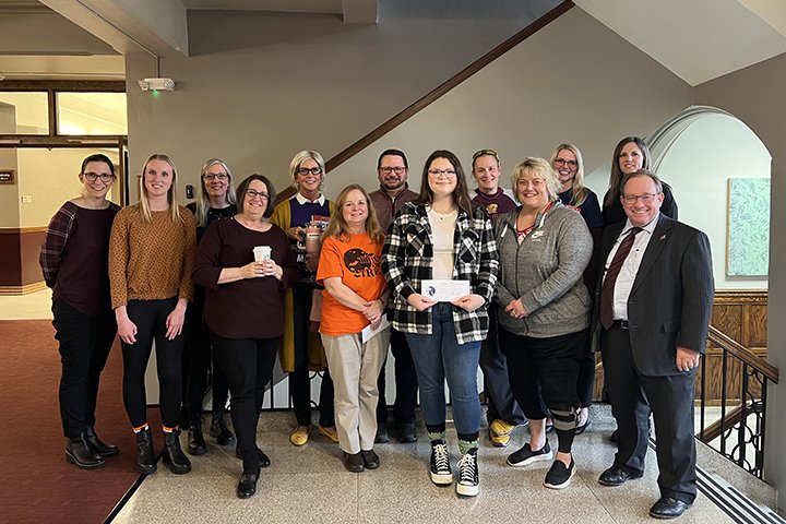 A dozen faculty, staff, students and President Davies pose for a photo inside Warriner Hall.