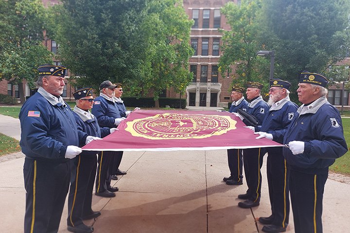 Eight veterans hold the CMU flag tightly, preparing to raise it on a flag pole near Warriner Hall.