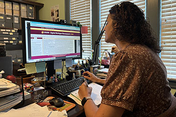 A woman in a floral blouse and with curly dark hair looks at a computer screen.