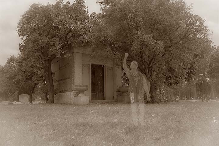 A shadowy figure stands in front of a mausoleum in a vintage styled picture.