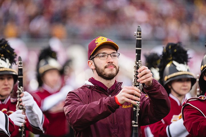 As the CMU alumnus stands holding a clarinet alongside members of the CMU marching band while on the turf at Kelly/Shorts Stadium.