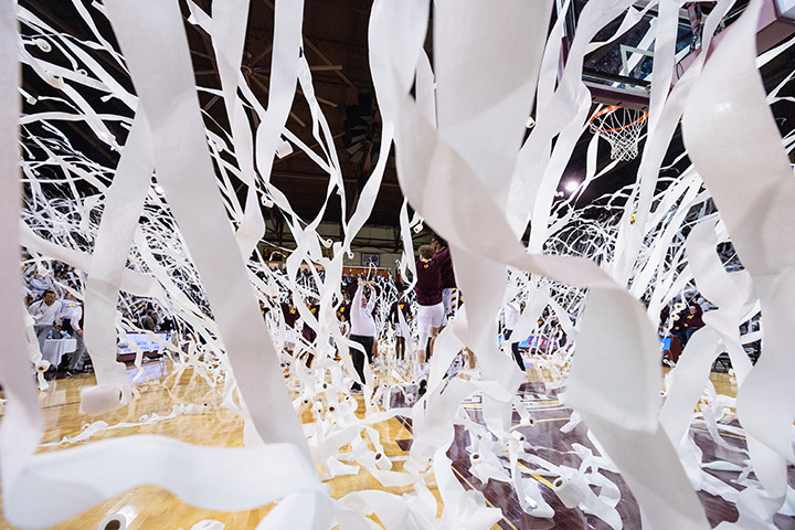 Toilet paper streams down onto a basketball court as President Davies stands on the court during a pre-game ceremony.