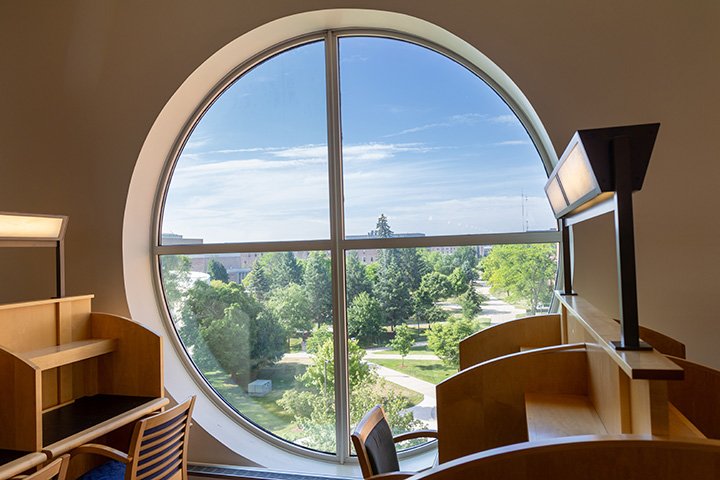 Next to two desks in the Park Library, a large circular window overlooks campus.