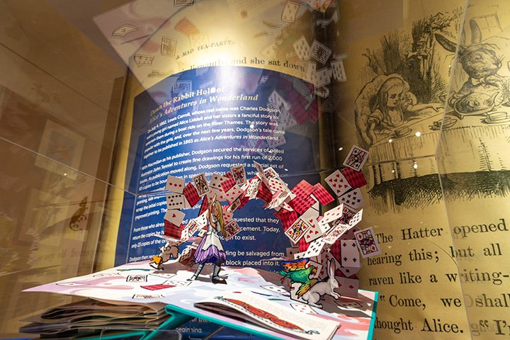 A pop-up book of Alice In Wonderland shows cards flying through the air, plus birds and a rabbit.