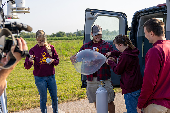 A group of CMU college students inflate a balloon using a large helium tank.