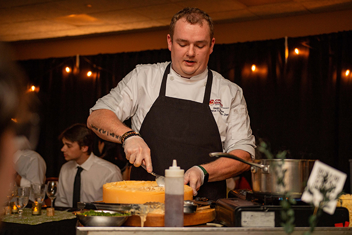 A CMU dining chef cuts into a some food, preparing to serve it at a fine dining event.