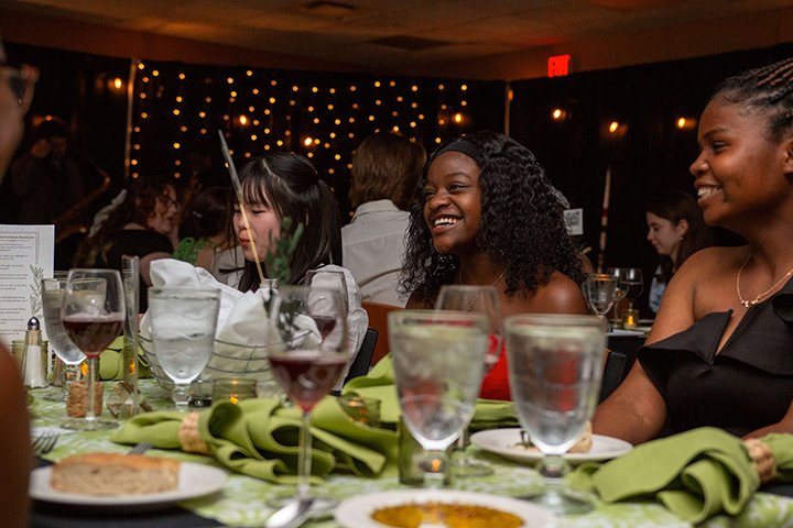 Students dressed in fancy clothes sit at a table enjoying a fine dining experience.