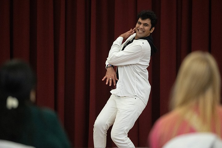 A male student in a white outfit takes part in the first Indian dance competition as a crowd of people watch.