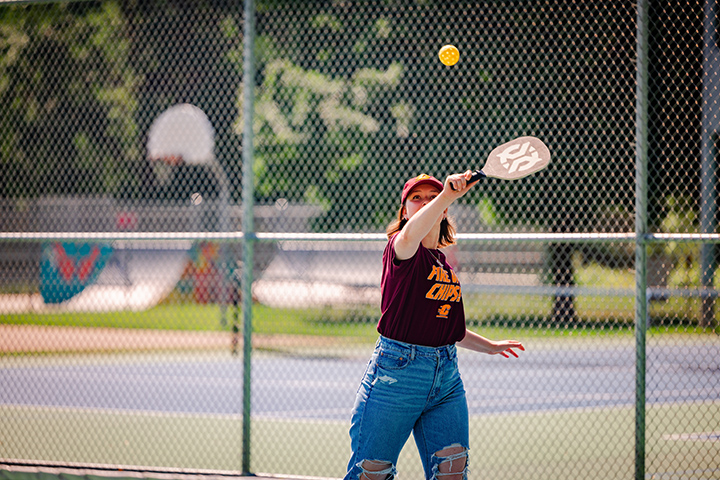 A young woman wearing a CMU hat and shirt plays pickleball.