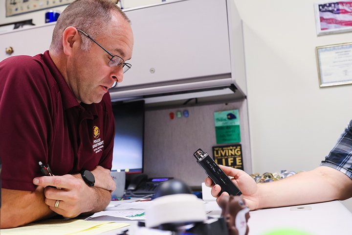 Lieutenant Cameron Wassman speaks into an audio recorder while sitting at his desk.