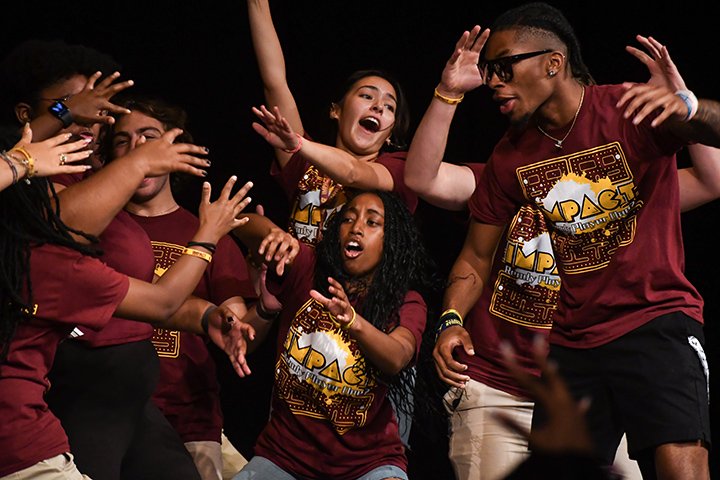 A large group of IMPACT participants huddles up while on stage during a pep rally.