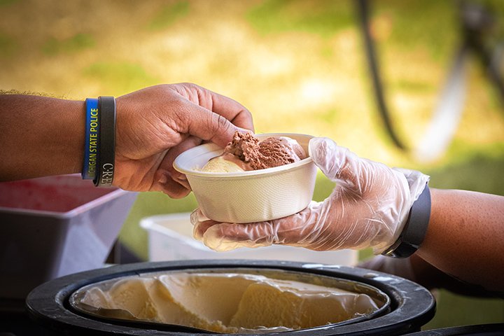 Closeup of a gloved hand giving a bowl of ice cream to another person.