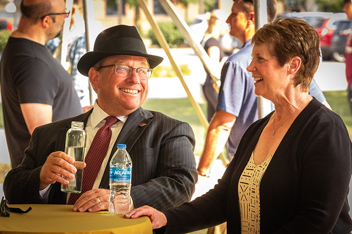 President Bob Davies holds a bottle of water and smiles at his wife as the two sit at a table.