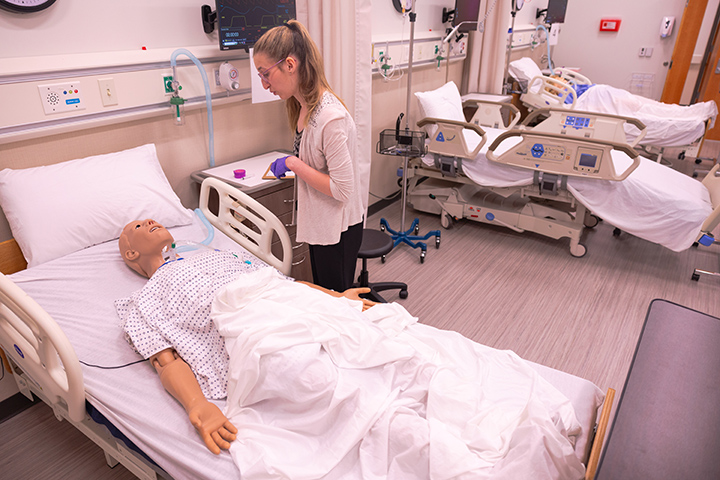 A health professions student examines a medical mannequin.