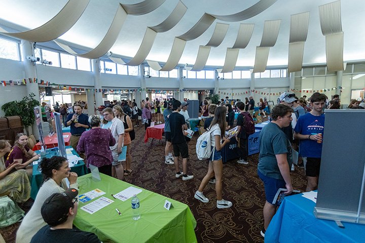 A wide angle view of the Rotunda Room where dozens of students speak with people at tables as part of the study abroad fair.