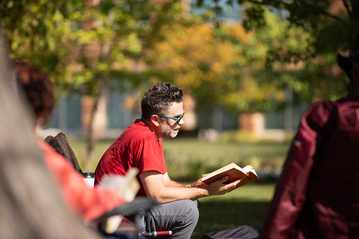 Professor Robert Fanning sits in a chair outdoors while reading a book.