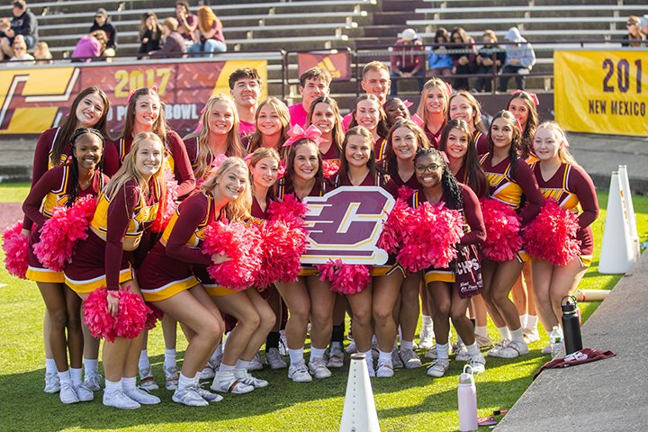 The CMU cheer team poses on the football field while holding a large Action C sign.